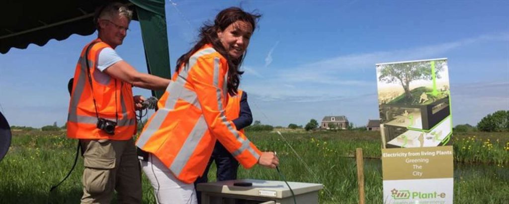 Gedeputeerde jacqueline verbeek nijhof met oranje jas bij stroomkastje in de berm
