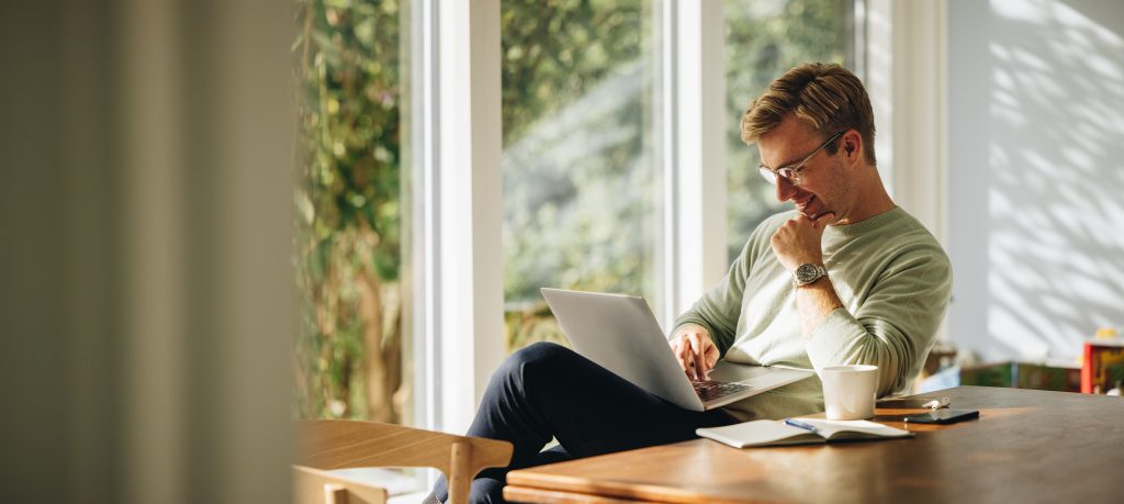 Adobe Stock man met bril werkt op laptop en kijkt blij